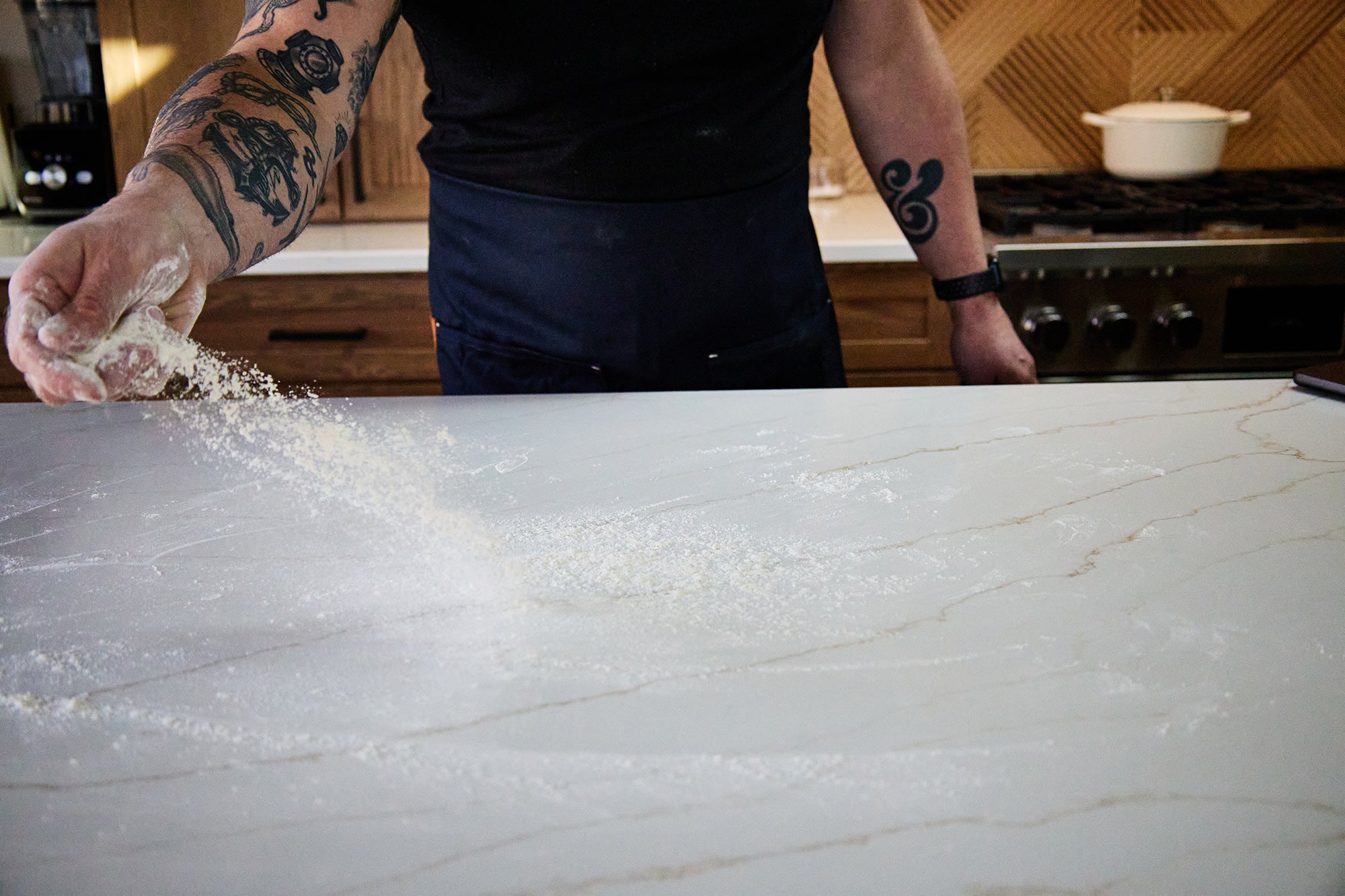 Person sprinkling flour on a quartz countertop in a kitchen.