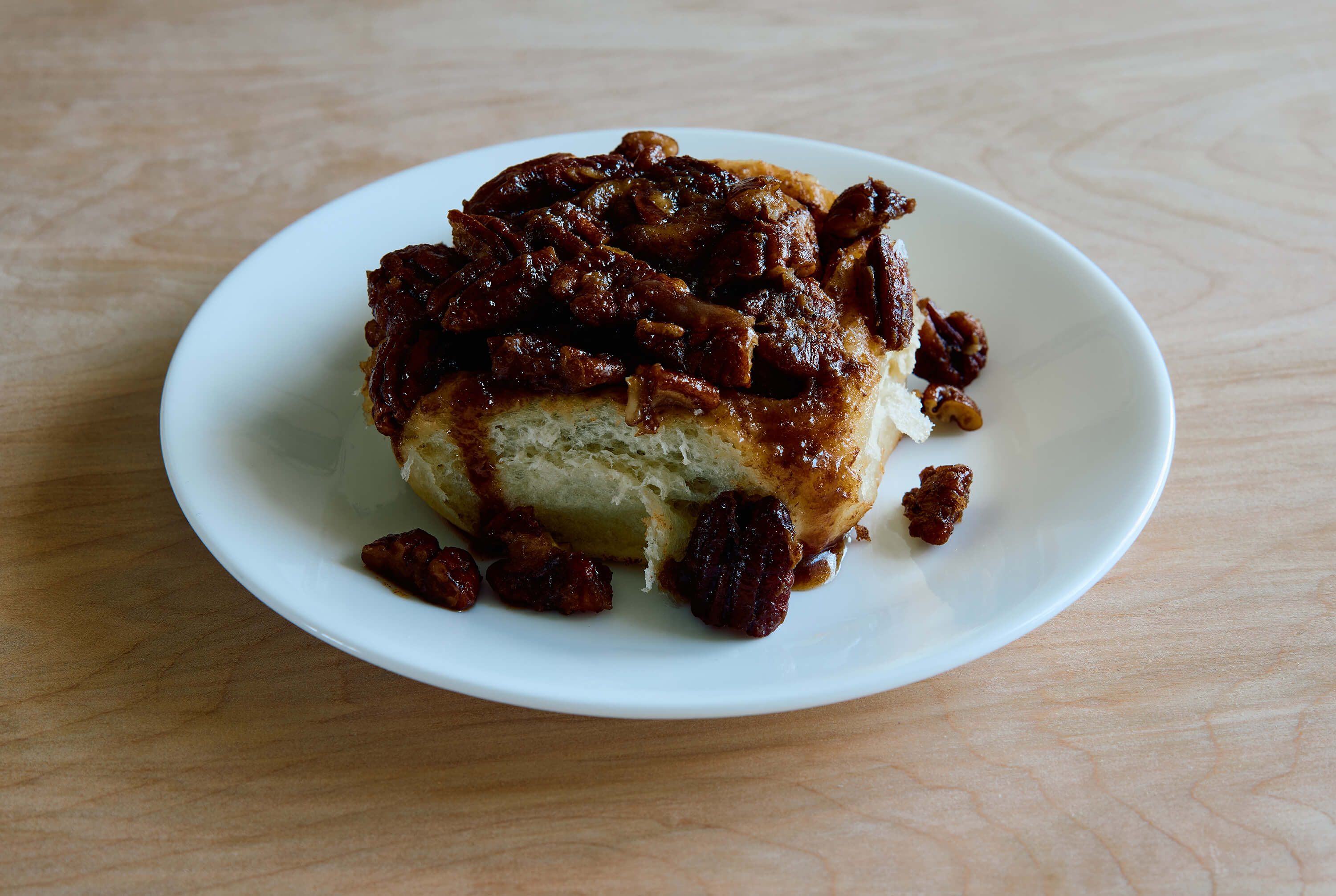 Cinnamon roll with pecans on a white plate on a wooden table